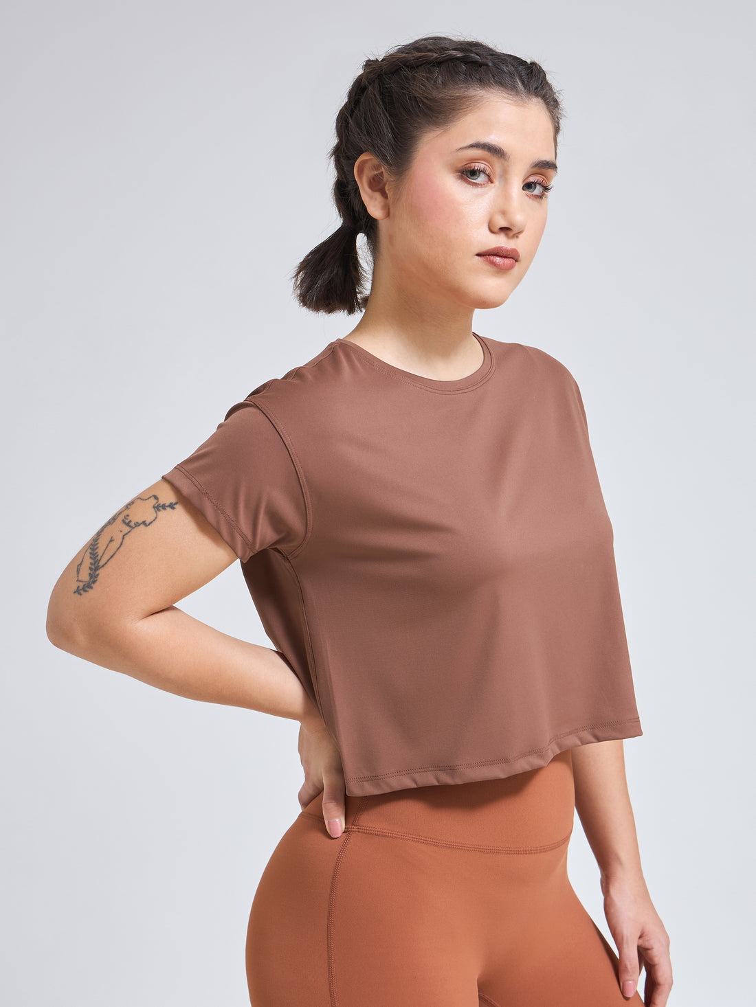 Woman wearing Infinito’s DryZone Minimalist Oversized Crop Top in soft taupe, styled with high-waisted leggings for a breathable and relaxed athletic look