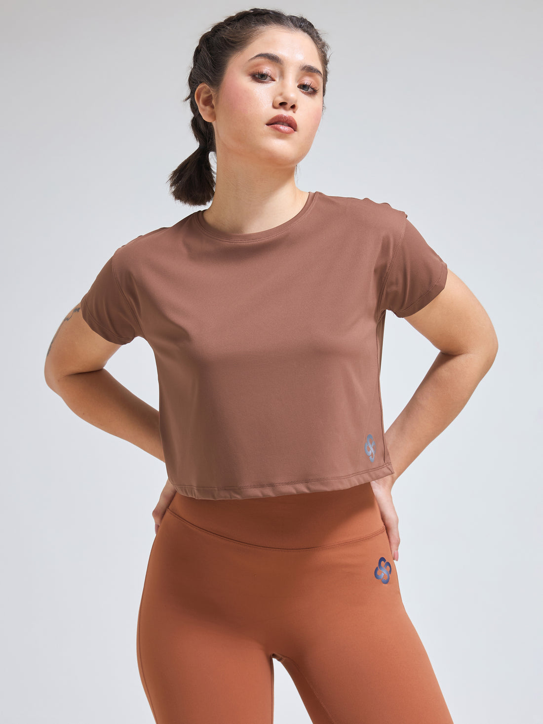 Woman wearing Infinito’s DryZone Minimalist Oversized Crop Top in soft taupe, styled with high-waisted leggings for a breathable and relaxed athletic look