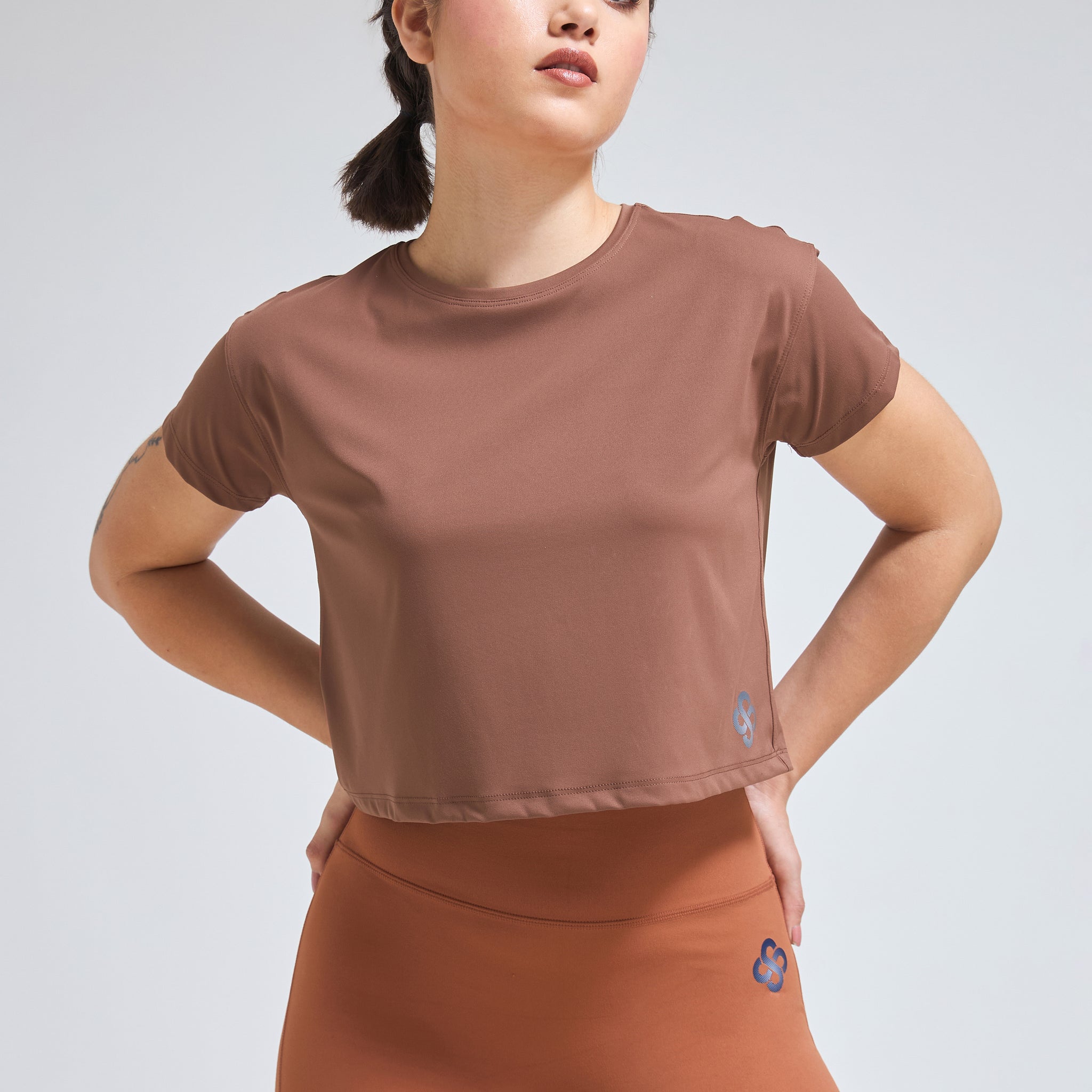 Woman wearing Infinito’s DryZone Minimalist Oversized Crop Top in soft taupe, styled with high-waisted leggings for a breathable and relaxed athletic look
