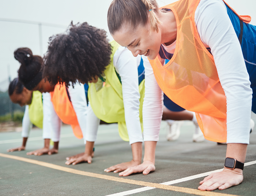 Women in athletic gear doing push-ups on an outdoor court during a workout session